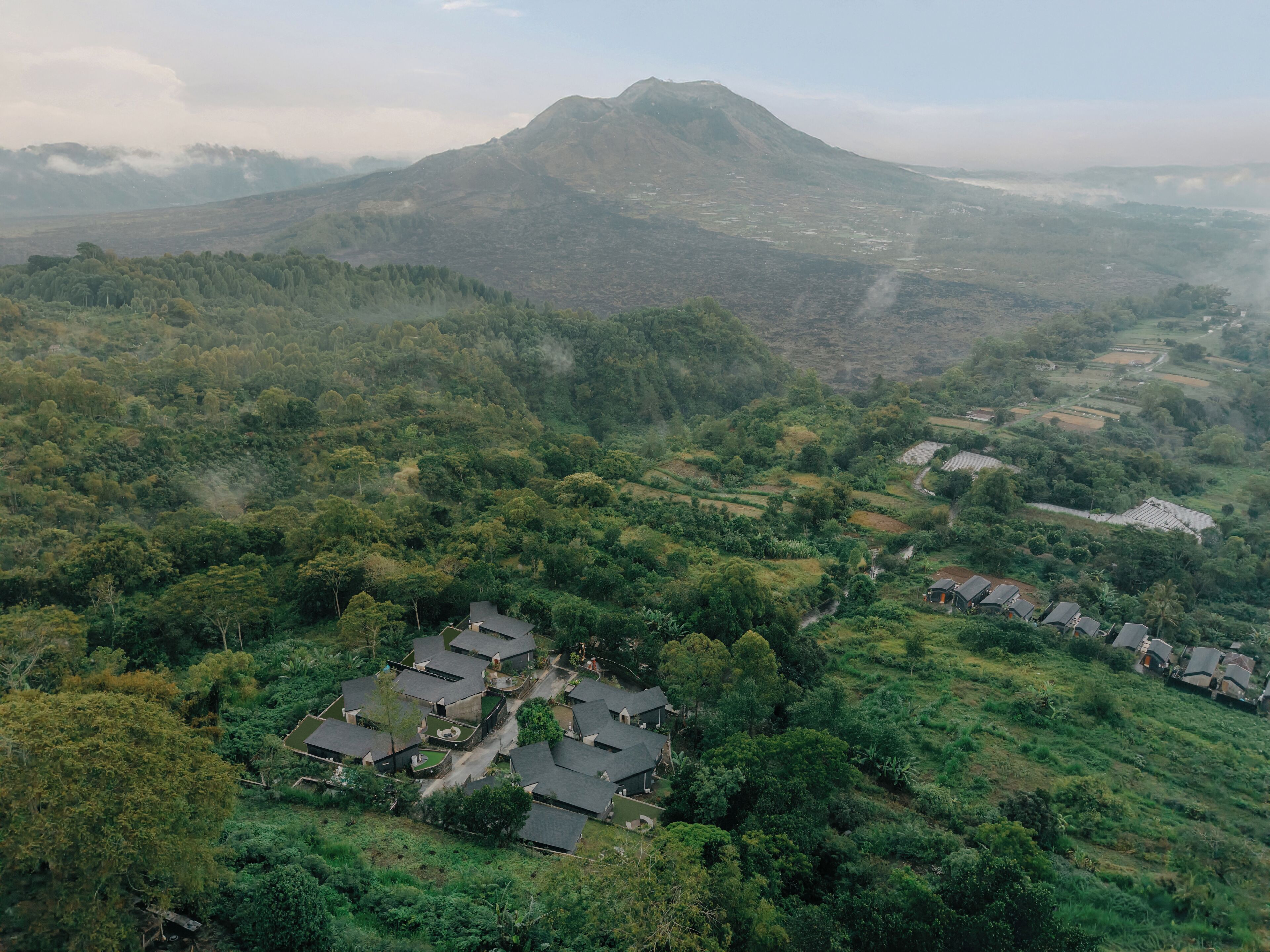 Un paisaje montañoso con un pueblo que presenta casas tradicionales de tejados inclinados, rodeado de abundante vegetación y campos en terrazas.