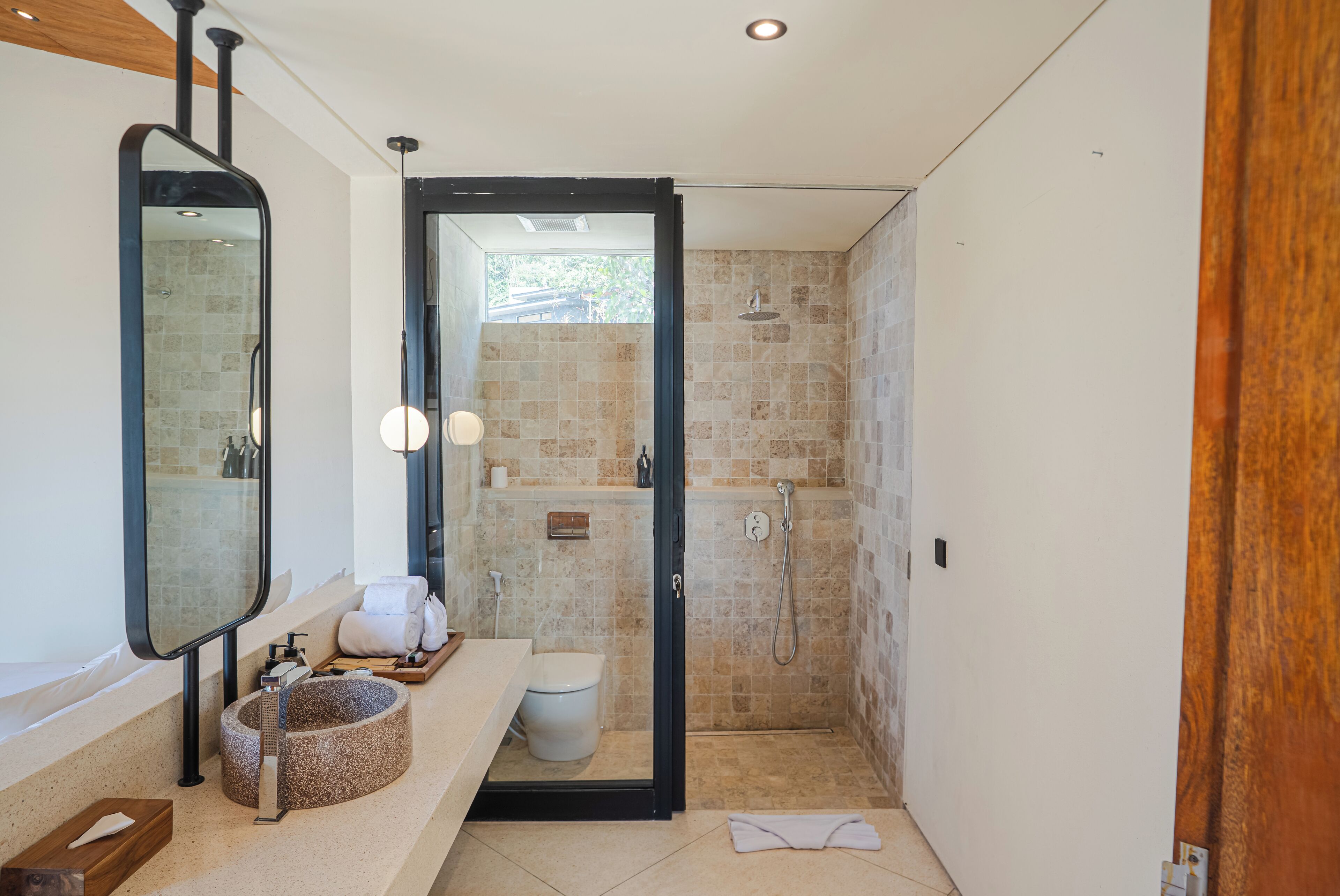 Un baño moderno con un lavabo redondo, un espejo grande, una ducha y un inodoro.