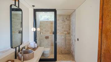 Un baño moderno con un lavabo redondo, un espejo grande, una ducha y un inodoro.