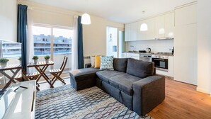 Un apartament modern amb zona de saló, petita cuina i balcó.