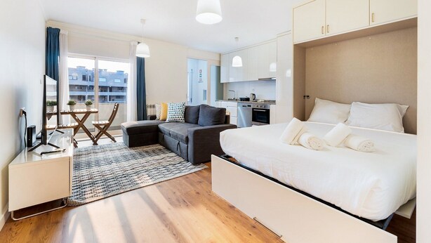 Habitació d'hotel moderna amb un llit gran, un sofà, una taula de treball i una cuineta.