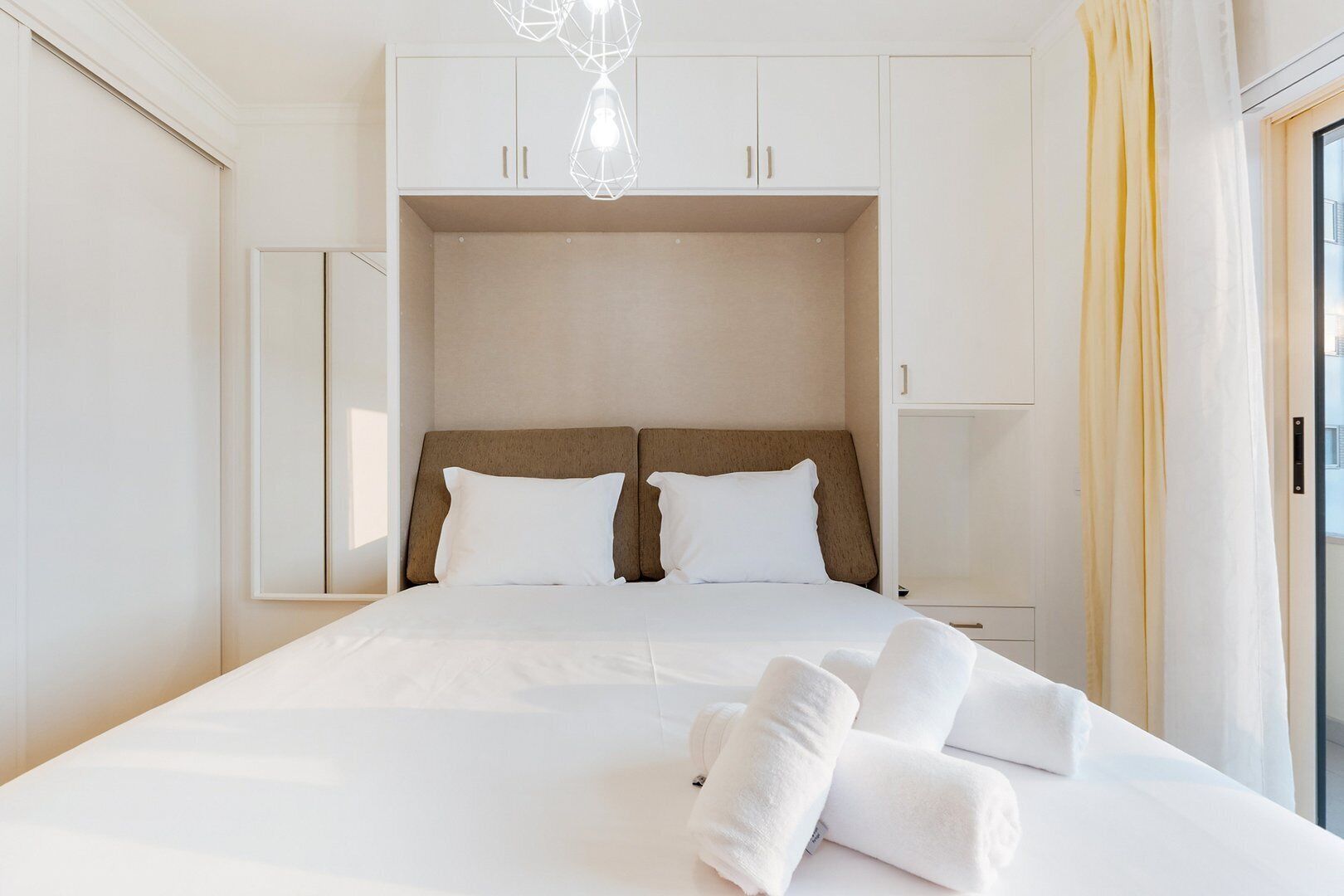 Une chambre d’hôtel avec un grand lit, deux tables de chevet, une armoire et un luminaire suspendu.