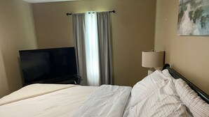 Une chambre d’hôtel avec un lit, une télévision, une lampe et une fenêtre avec des rideaux.