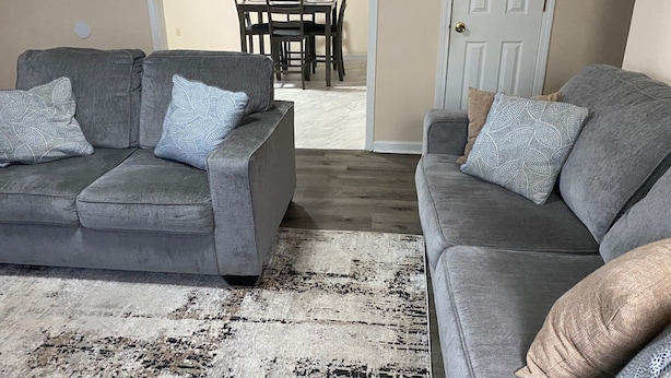 Un salon avec deux canapés gris, un tapis à motifs et un coin repas comprenant une table et des chaises.