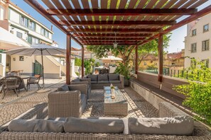 Une terrasse extérieure aménagée avec des meubles en osier, une table à plateau en verre et une structure en forme de pergola.