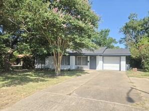 Einbungalow mit Garage, Auffahrt und einem großen Baum davor.