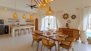 A modern kitchen with a central island, wooden chairs, and hanging wicker light fixtures. - Villa Nokanhui by Pertama Stay (Canggu)