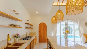 A modern kitchen with wooden shelves, a large sink, and pendant lights. - Villa Nokanhui by Pertama Stay (Canggu)