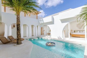 Un espace piscine avec des chaises longues, un palmier et un jacuzzi rond.