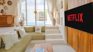 A modern living room with a green sofa, a wooden coffee table, and a large TV screen displaying the Netflix logo. - Villa Nokanhui by Pertama Stay (Canggu)