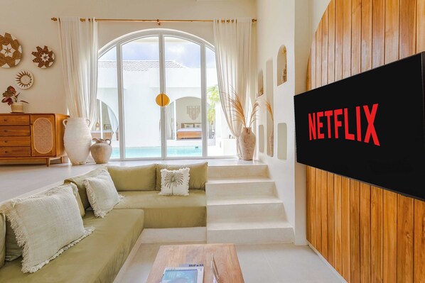 A modern living room with a green sofa, a wooden coffee table, and a large TV screen displaying the Netflix logo.
