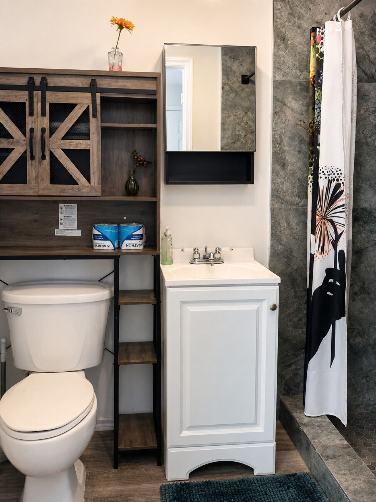 A bathroom with a white toilet, a sink with a mirror above it, and a shower curtain with a floral pattern.