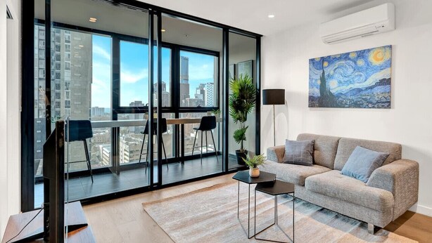 Ein modernes Wohnzimmer mit einem großen Schiebeglasfenster, das auf einen Balkon führt, einem grauen Sofa, einem Couchtisch und einem Gemälde von einer Sternennacht.
