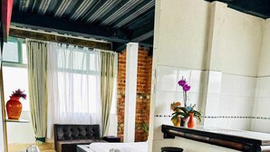 A modern living room with a grey sofa, a small kitchen area, and a dining table. - Villa Tikuna (San Sebastian de Mariquita)