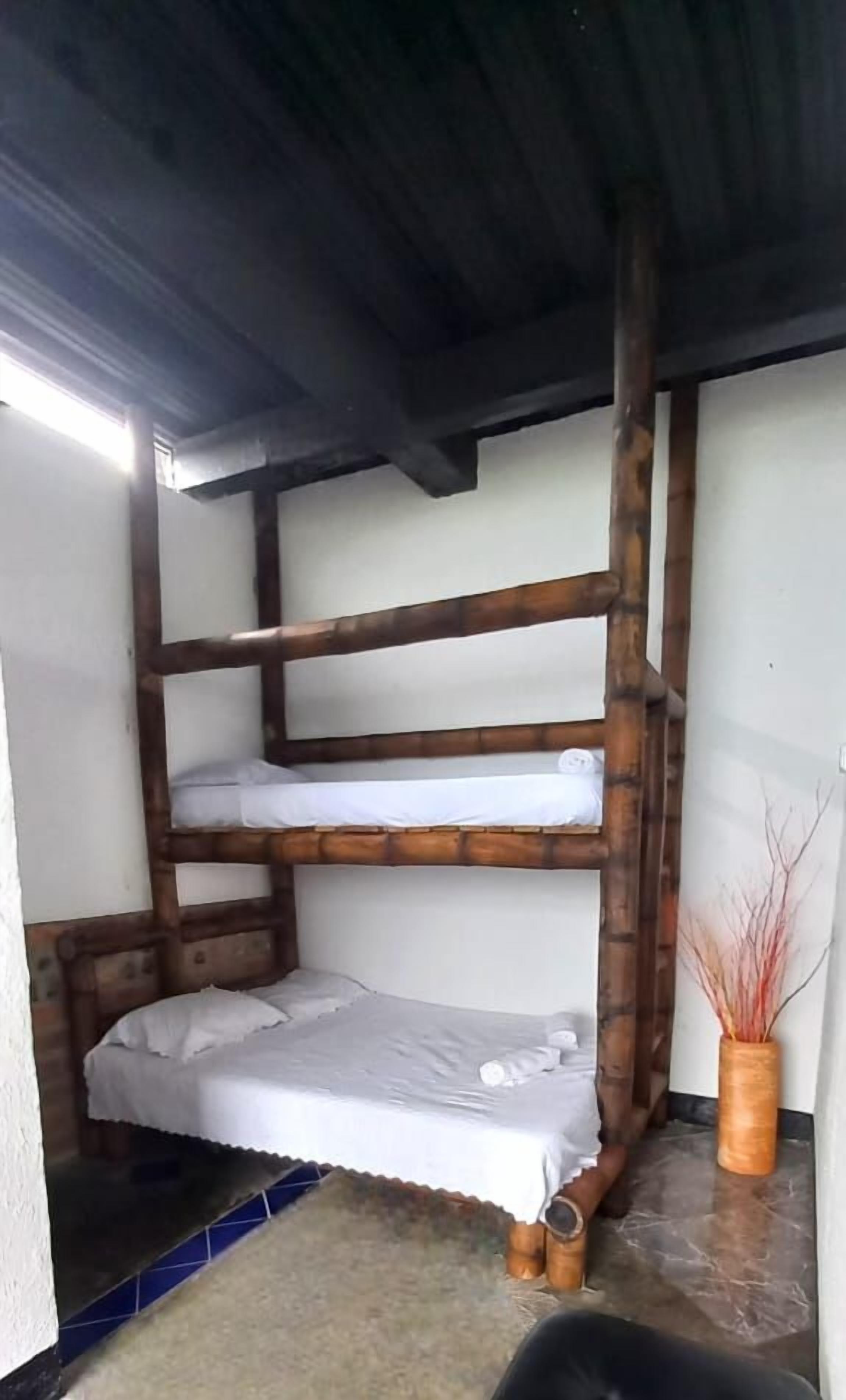 Quarto com beliche, uma cadeira preta e um vaso com plantas secas.