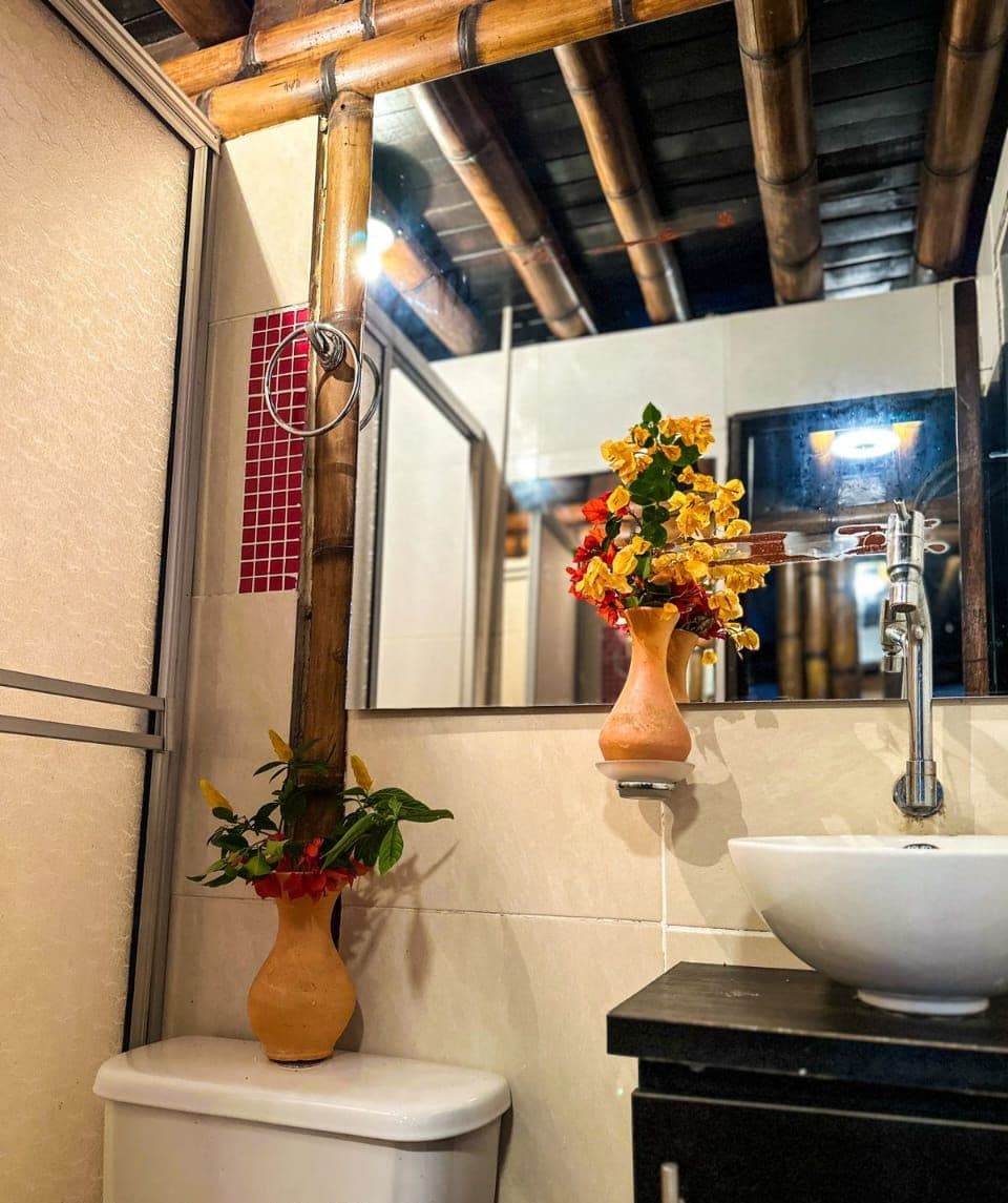 A bathroom with a toilet, a sink, and a mirror. There are two vases with flowers on the wall.