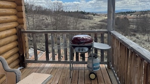 Een houten terras met een barbecue en een tafel, met uitzicht op een bergachtig landschap.
