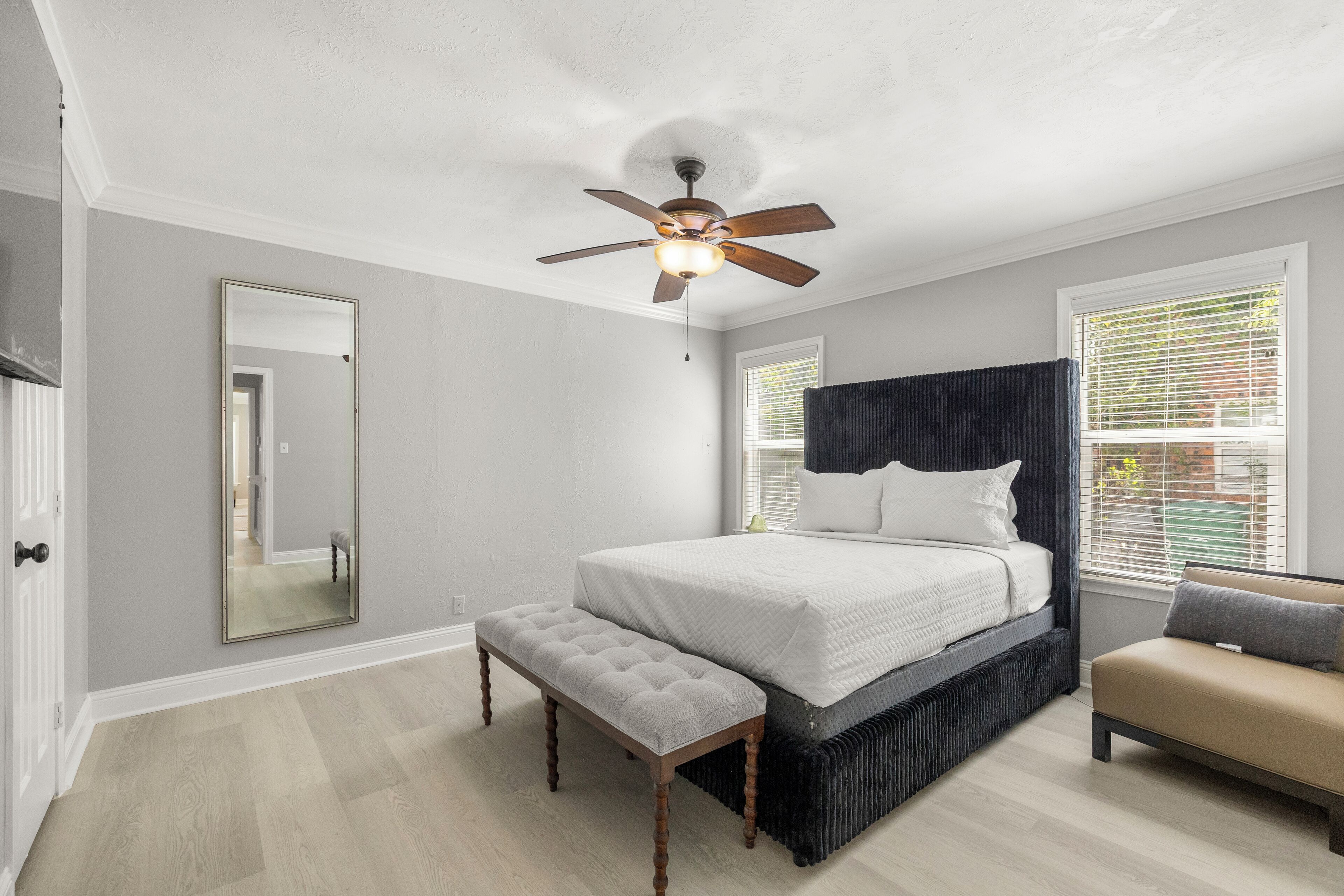 Une chambre à coucher comprenant un lit, un banc, un ventilateur de plafond et une fenêtre avec des stores.