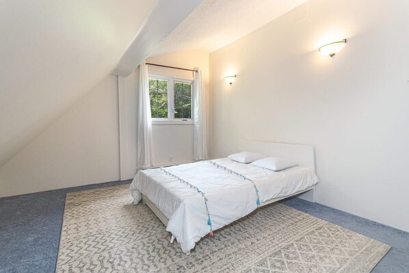 A bedroom with a bed, a window with curtains, and a wall-mounted light fixture.
