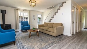 A living room with a beige sofa, blue armchair, and a small coffee table. A staircase is visible to the right.