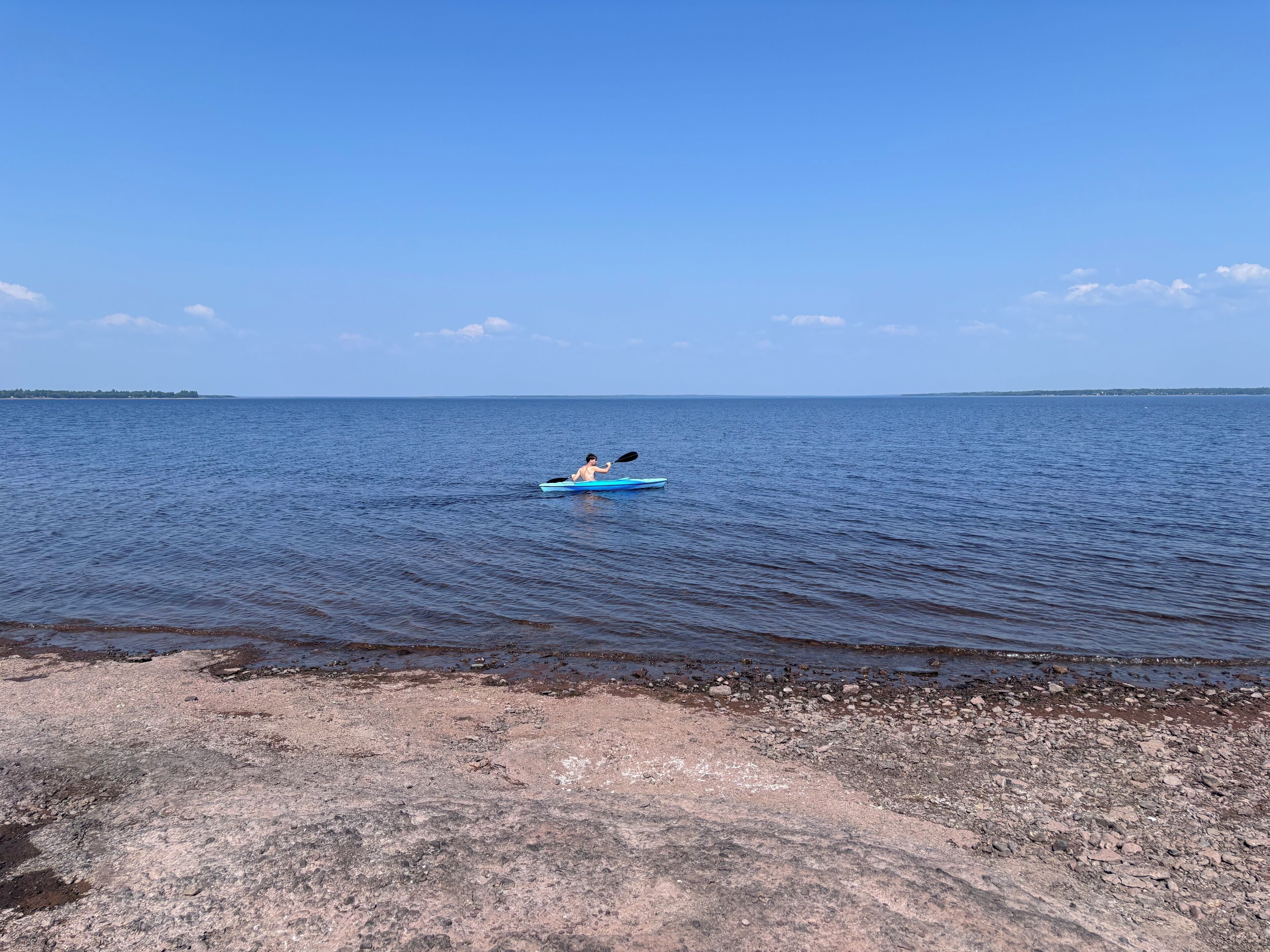 A kayaker on a calm body of water with a rocky shoreline in the foreground.