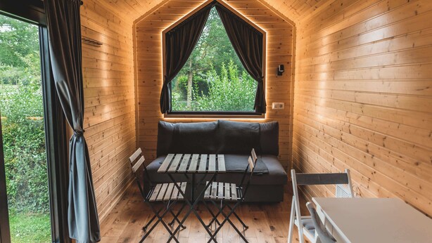 Interior acogedor de una cabaña, con paredes de madera, una ventana con cortinas, un sofá y una mesa.