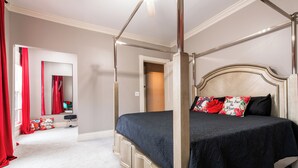 Una cama con dosel adornada con una colcha oscura y almohadas estampadas, cabecera de madera y suelo cubierto de alfombra blanca.