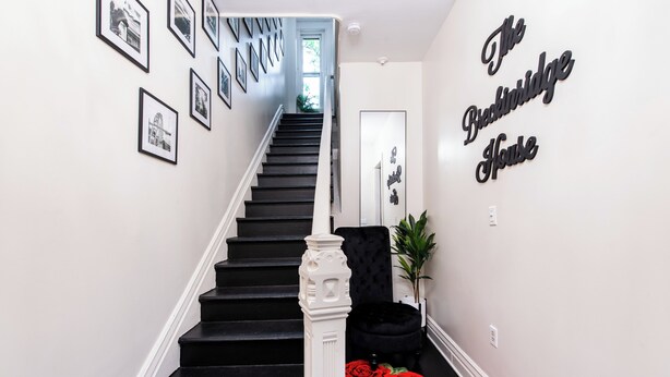 Una escalera con escalones negros y balaustres blancos que lleva a una plataforma con una silla negra y una planta.