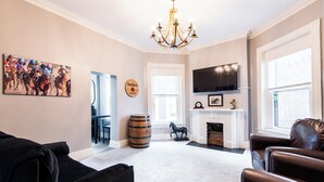 Un salón con chimenea, televisor montado y un cuadro grande de carreras de caballos.