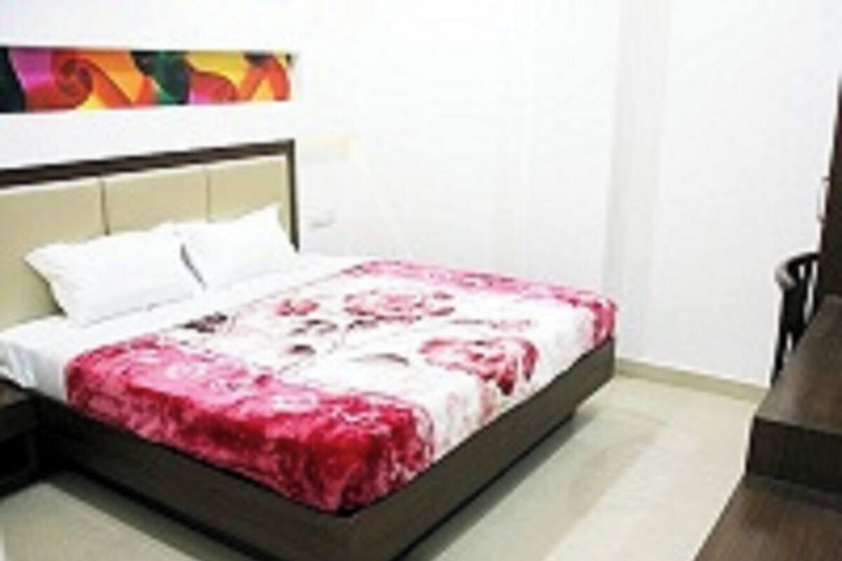 Ein ordentlich gemachtes Bett mit einem gemusterten Überwurf in einem Zimmer mit einem weißen Kopfteil und einem farbenfrohen, abstrakten Kunstwerk darüber.
