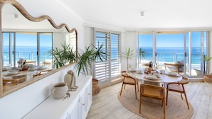 A dining area with a view of the ocean, large windows, and a round table with chairs.