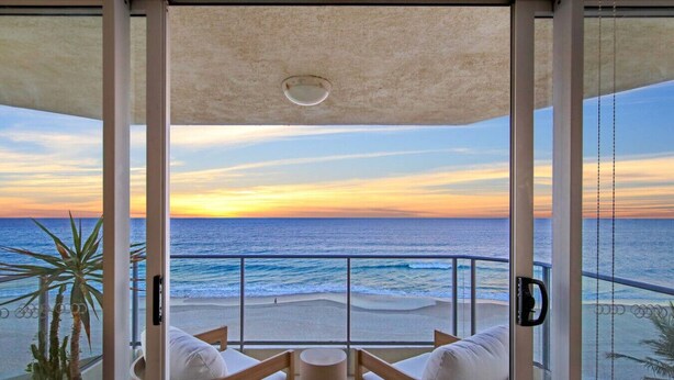 A balcony with a view of the ocean at sunset, featuring a wooden chair and a small table.
