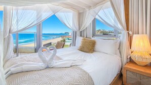 A bed with a canopy, a view of the beach, and a lamp on a nightstand.