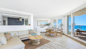 A spacious living area with a large sofa, a dining table with chairs, and a view of the ocean through large windows.