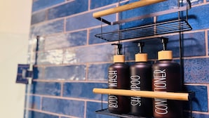 Casa de banho com parede azulejada em azul e uma prateleira de metal preta com garrafas rotuladas como 'Body Wash', 'Shampoo' e 'Conditioner'.