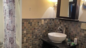 Een badkamer met een betegelde spatwand, een wit wastafelmeubel, een spiegel en een douchegordijn.