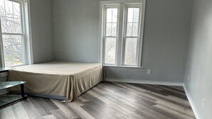 Een kamer met een groot raam, een bed en een houten vloer.
