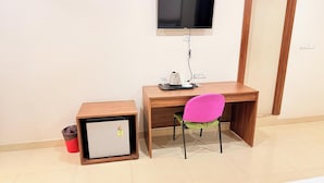 A small room with a wooden desk, a chair, a television mounted on the wall, and a small refrigerator. - PARADISE PREMIUM (Bhubaneshwar)