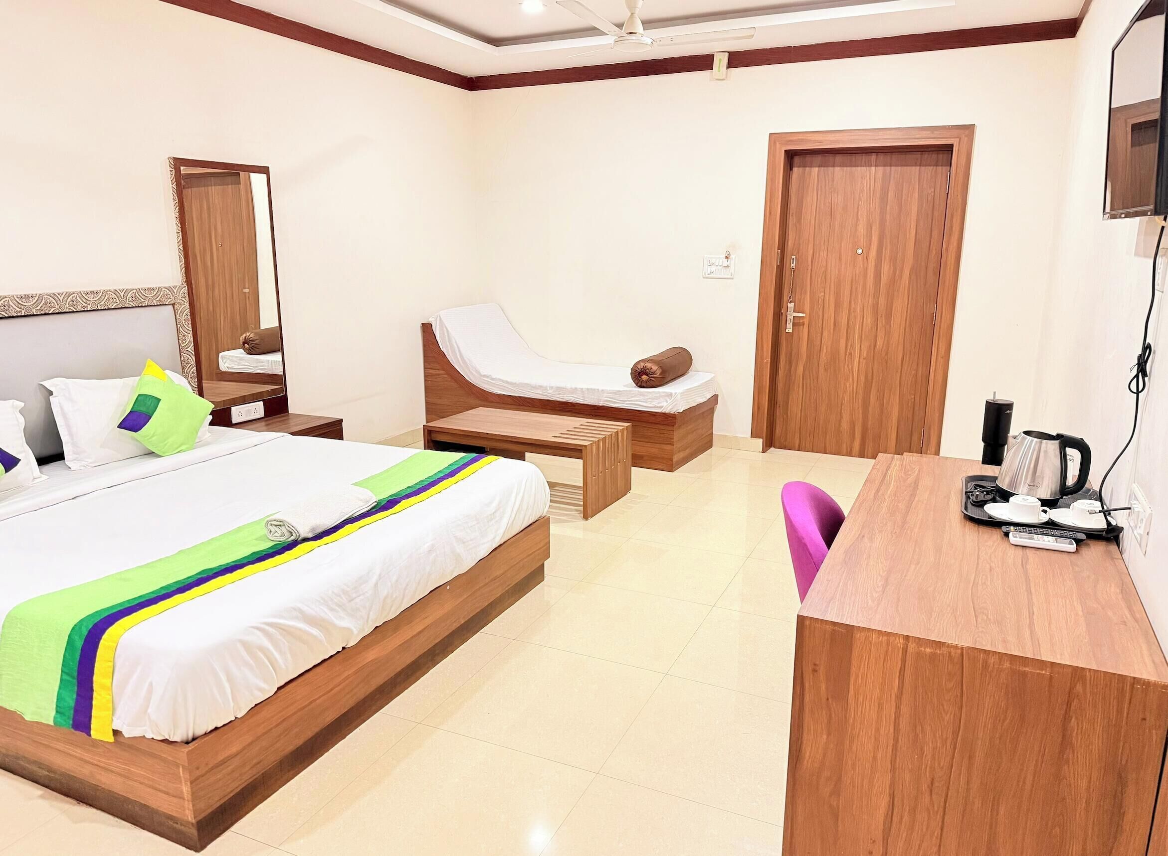 A hotel room with a large bed, a desk, a chair, a mirror, and a door.