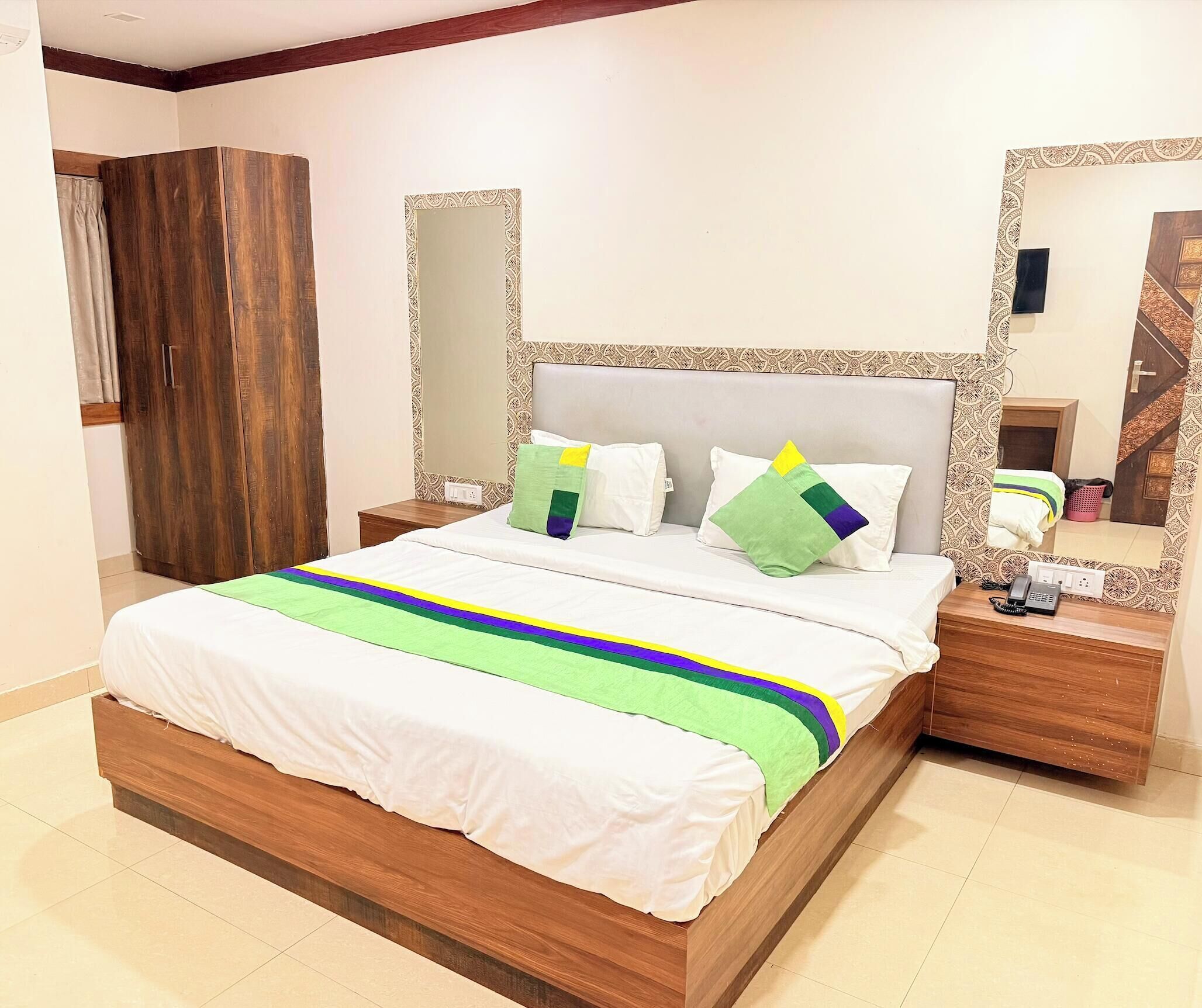 Una cama bien hecha con colcha a rayas, cabecera de madera y dos mesitas de noche con teléfono y lámpara.