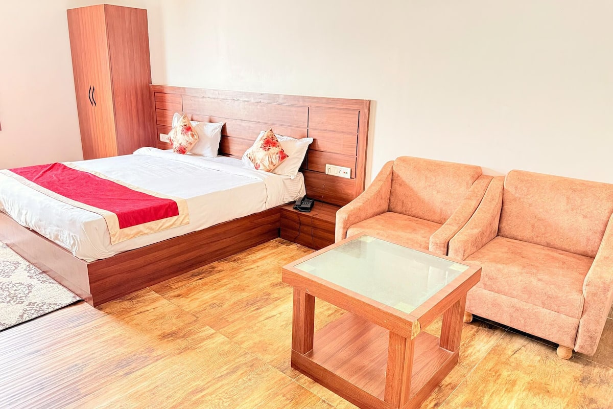 A bedroom with a bed, a wooden wardrobe, a sofa, and a glass-top coffee table.