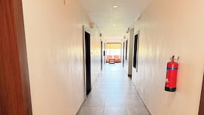 A hotel hallway with a fire extinguisher mounted on the wall, a sofa in the background, and a tiled floor. - PARADISE PREMIUM (Bhubaneshwar)