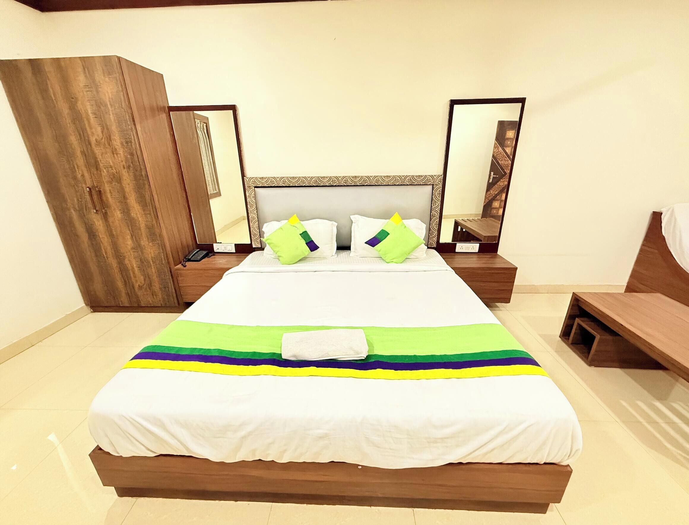 Una cama bien hecha con cubrecama a rayas, dos mesitas de noche con lámparas, un armario de madera y un espejo grande en la pared.