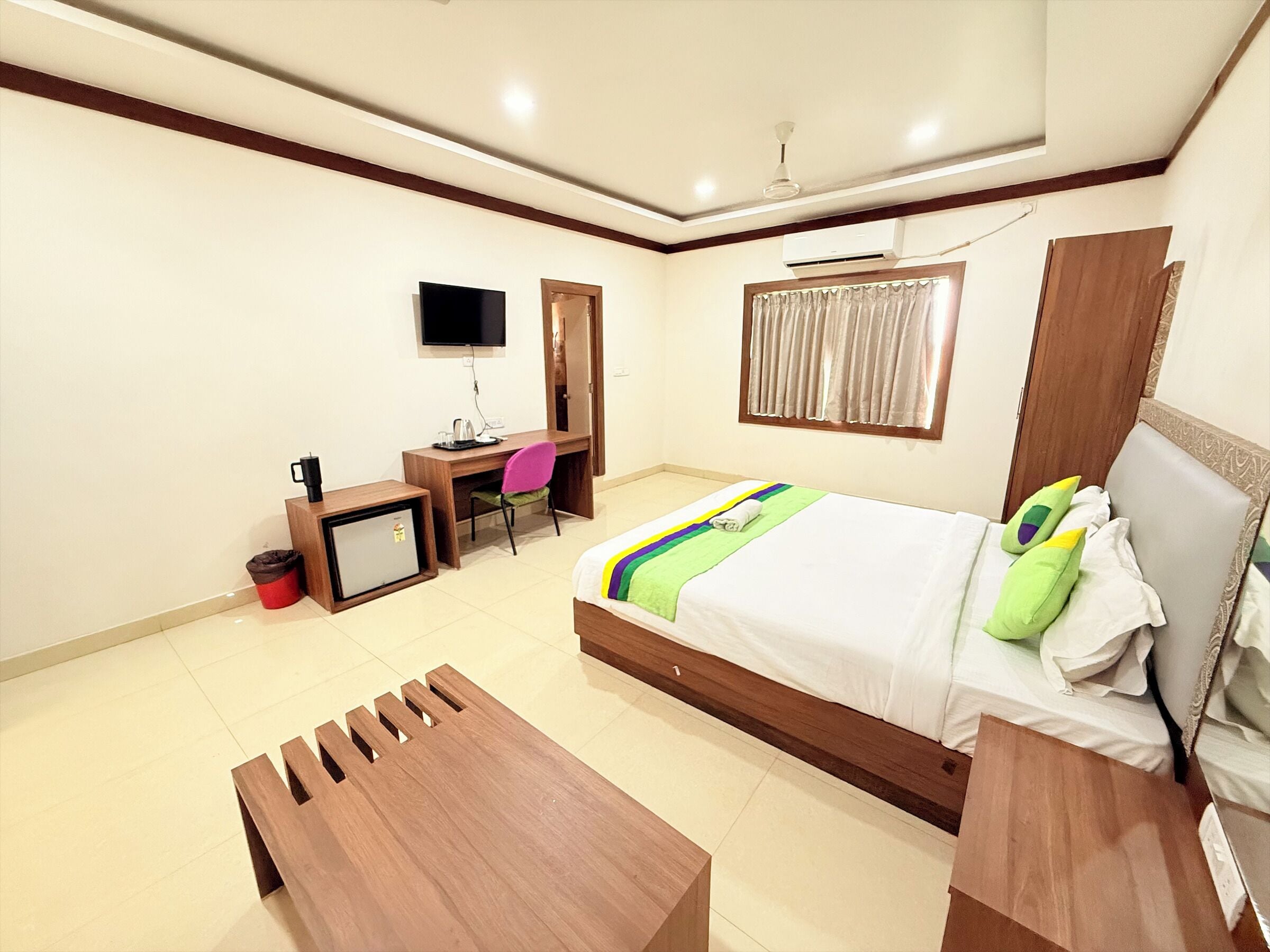 A hotel room with a bed, a desk, a chair, a TV, and a ceiling fan.