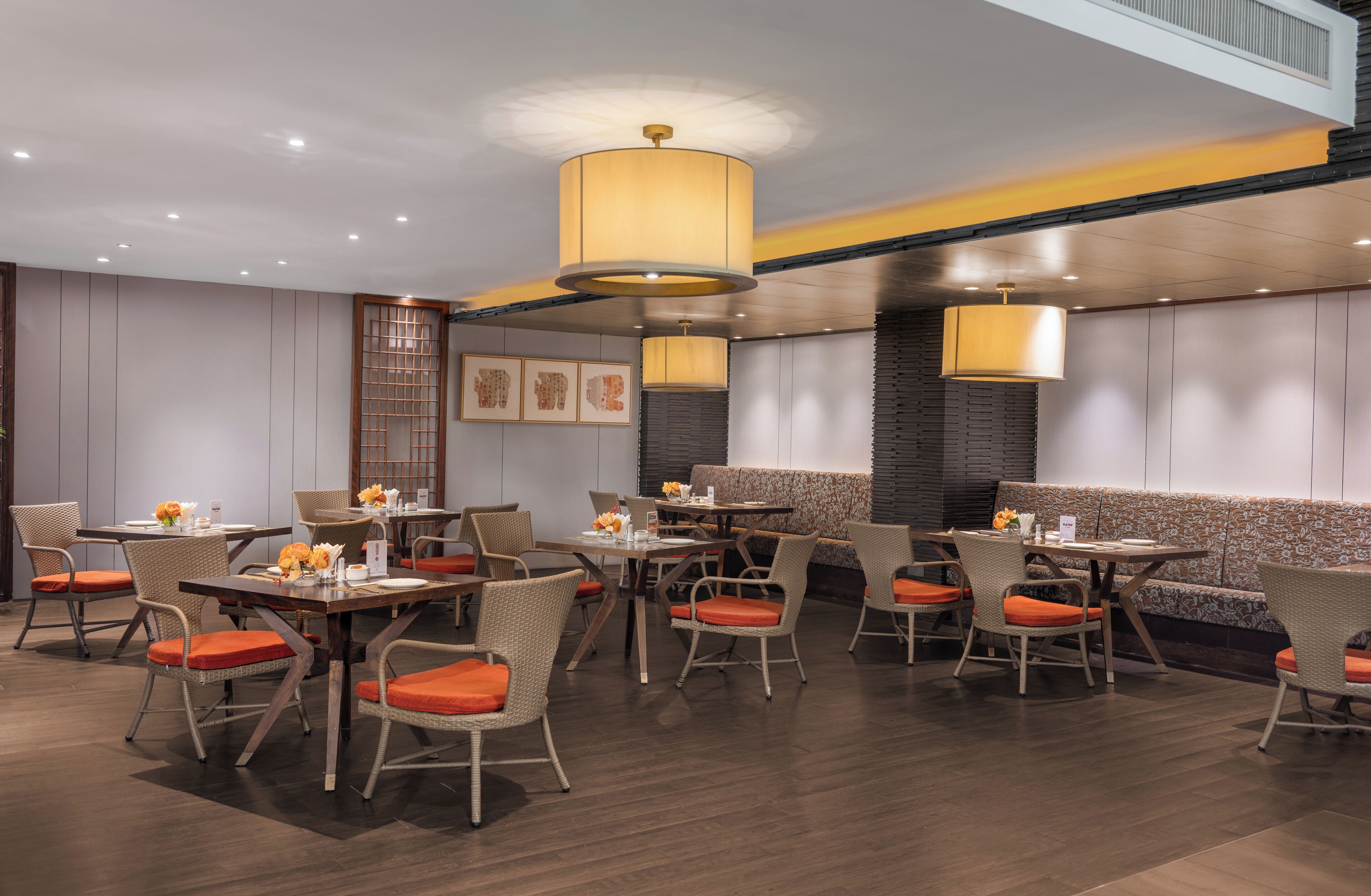 A restaurant with multiple tables and chairs, featuring a modern design with wooden flooring and orange cushions.