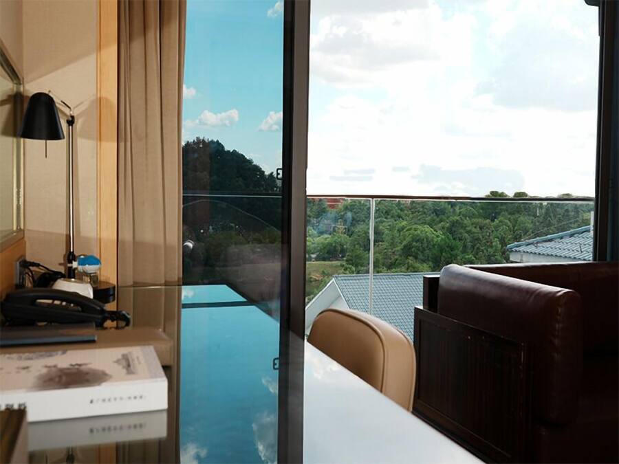 A hotel room with a large window offering a view of a green landscape and traditional buildings.