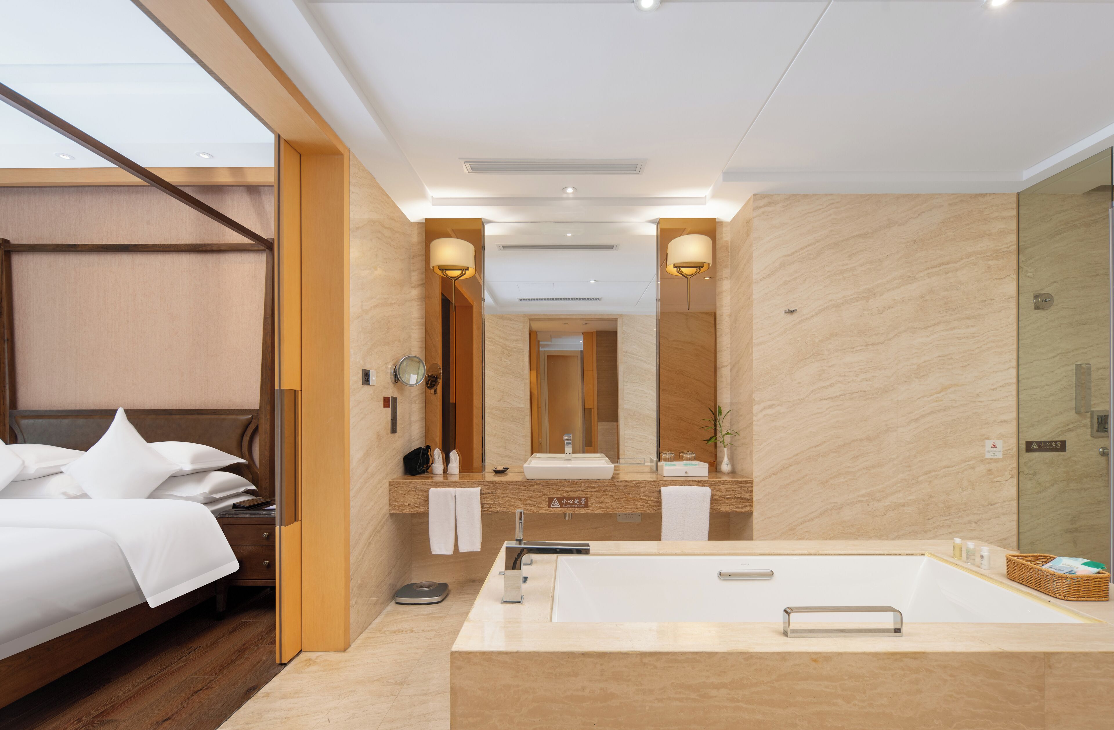A modern hotel room with a large bed, a bathroom with a bathtub, a mirror, and a wooden floor.