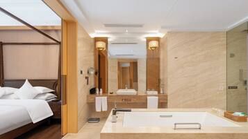 A modern hotel room with a large bed, a bathroom with a bathtub, a mirror, and a wooden floor.