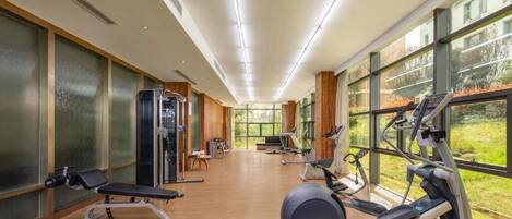 Un gimnasio con equipamiento de ejercicio, ventanas amplias y suelo de madera.