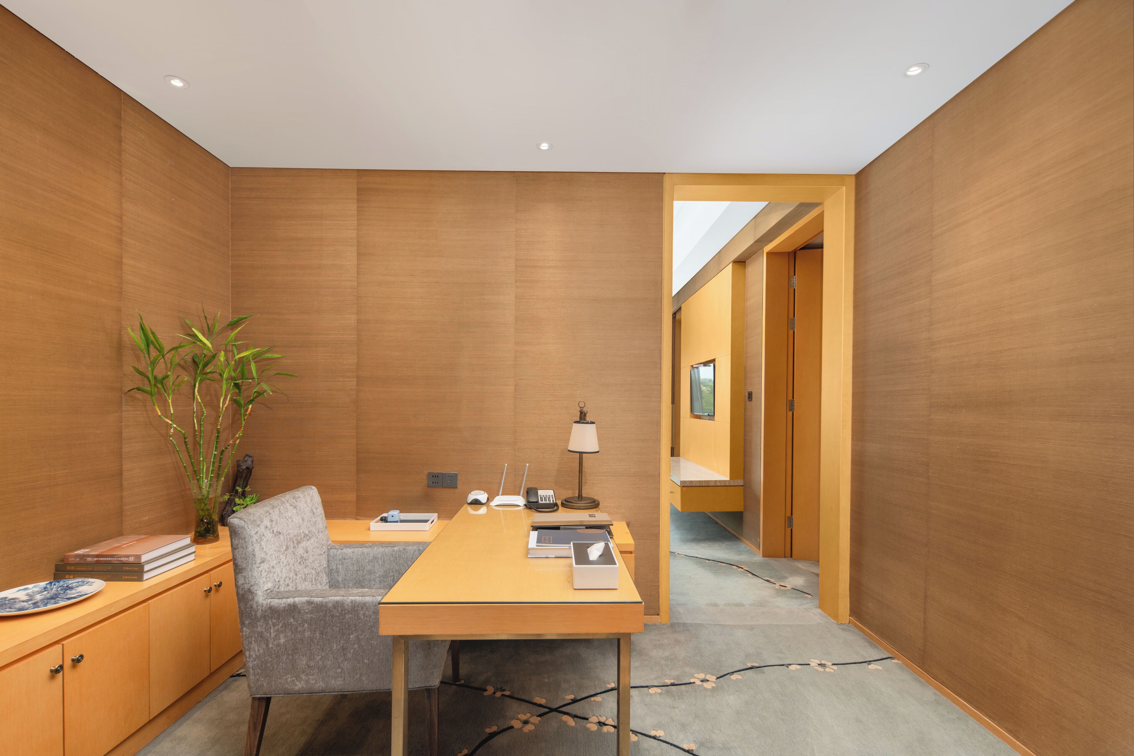 Una habitación moderna con una pared de madera, un escritorio con silla, una lámpara, una planta y una estantería.